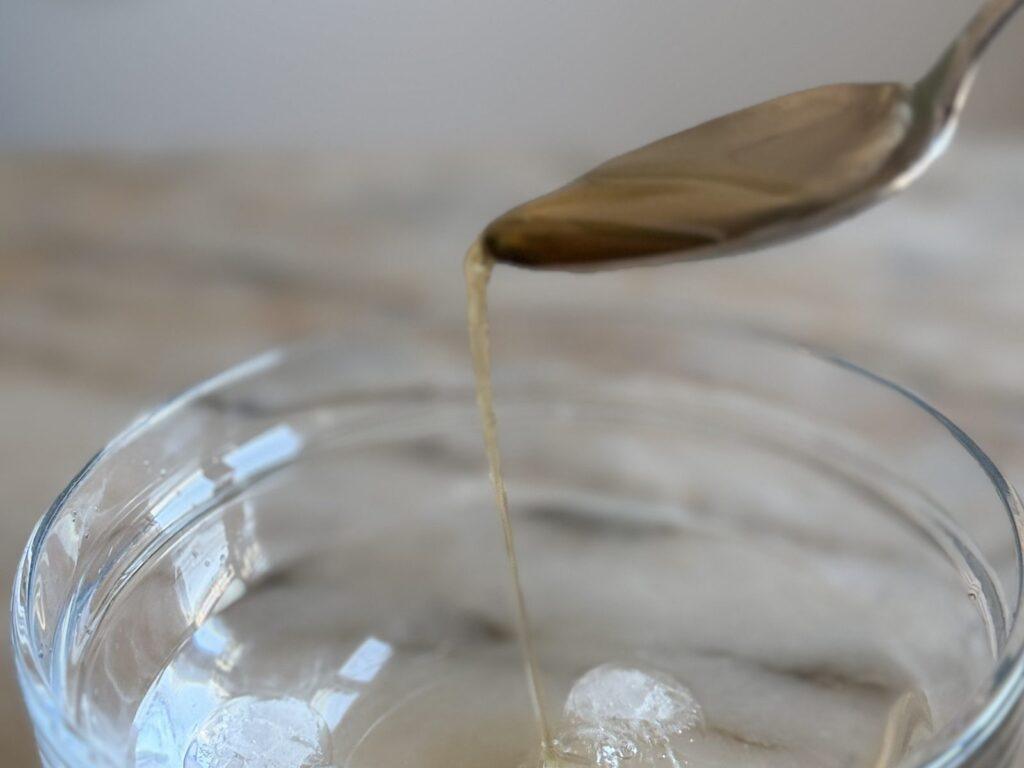 Hot sugar syrup dripping from a spoon into a glass bowl of ice water for the cold water test